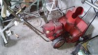 Side view showing the red metal body of the vintage snow blower including the engine and chute for snow discharge.