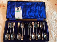 View of eight silver plate demitasse spoons and a pair of silver plate sugar tongs in original fitted case with blue satin and velvet lining.