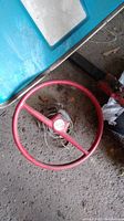 Full view of the red Atwood steering wheel resting on the floor showing round wheel and attached wiring.