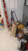 Photo of various tools including levels, bow saws, duct tape, punch pliers, coiled cords, Dewalt sander, and Black & Decker hedge trimmer in basement setting.