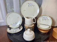 Five hand-painted playing card-themed porcelain plates with gilt rims arranged with a mid-century white porcelain creamer and covered sugar bowl on a black surface.