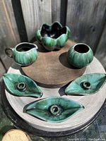 Top-down image showing all six pottery pieces with green and black glaze set on a round surface outdoors in natural light.