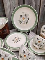 Set of plates, teacups and saucers displayed showing the Wild White Rose floral pattern with green border.