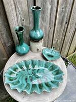 Photo of 4 ceramic pottery pieces: two vases, scalloped tray and leaf bowl on wooden surface against outdoor background