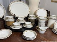 Photo displaying the oval tray, teacups with saucers, berry bowls and other plates arranged on a tabletop mixing wood and black stands for display.