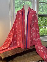Front side of handmade silk sarong draped on mannequin showing vibrant pink fabric with white floral and dotted patterns and coral red border with blue stripe.