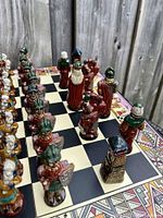 Side close-up of red and green glazed Conquistador side chess pieces arranged on board including pawns and prominent king piece with white beard.
