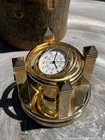 Front angled view of solid brass celestial spinning desk clock on a wooden surface showing Roman numeral dial and pyramidal pillar tops.