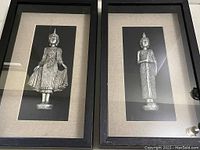 Pair of black box frame art pieces each with a silver-tone Buddhist figurine on linen matting.