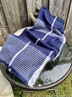 Calvin Klein acrylic wrap throw blanket displayed on glass table, showing navy and white houndstooth and plaid pattern with white fringe edges.