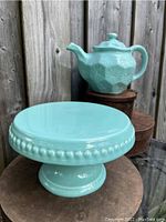 Ceramic light turquoise cake tray with bead detailing on the edge and pedestal base shown alone.