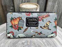 Front side of grey Loungefly Harry Potter wallet showing colorful Harry Potter motifs including sorting hat, broomstick, and potion bottles with a black Harry Potter Loungefly metal logo plate.