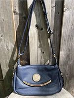 Front view of the Michael Kors crossbody handbag showing indigo blue pebbled leather, circular MK logo medallion, and gold-tone curved bar detail.