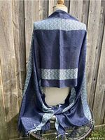 Fringed blue and gray viscose scarf draped over mannequin, showing back side with geometric patterns and fringe at the bottom.