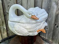 Side view of the white ceramic swan tureen showing detailed feather texture, orange beak and feet, with lid separating at the mid-body.