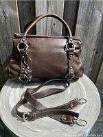 Front view of chocolate brown pebbled leather bag with attached decorative charm and separate crossbody strap laid out.