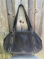 Front view of dark brown leather Cole Haan handbag showing oval shape, stitched leather, and gold-tone hardware.