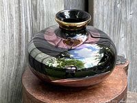 Front angled view showing the bulbous shape, reflective dark glaze, and gold rim of the vase