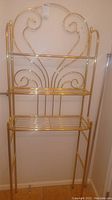 Full view of the brass over the toilet bathroom shelf showing the metal frame and shelving with decorative swirls.