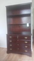 Front view of the solid dark wood cabinet showing upper shelving and lower drawers with brass handles and central lock keyhole.