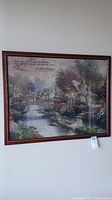 Wide view of detailed Thomas Kincade tapestry showing village scene with river and stone bridge, framed in dark wood.