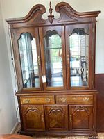 Full frontal view of wood hutch showing upper glass display cabinet with three glass doors, decorative carved wood top, and lower wooden cabinet with drawers and doors.