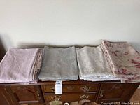 Four folded curtains including pink lace, white lace, light green lace, and floral pink sheers placed on wooden surface.