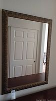 Full view of rectangular wall mirror with dark carved wooden frame reflecting a white door