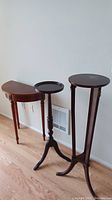 Three wood furniture pieces: one semi-circular table and two tall plant stands, all dark wood finish and traditional style.