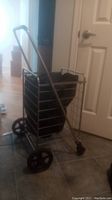 Side angle view of metal framed rolling cart showing black fabric bag, large rear and smaller front wheels, and upright handle.
