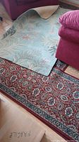 Image showing two of the wool area rugs, one light blue with floral pattern and the other a traditional red design, both needing cleaning.