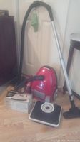 Red Simplicity JILL.10 canister vacuum with hose and metal wand, Dirt Devil hand vacuum in background, Terraillon scale with black platform and round dial in foreground.