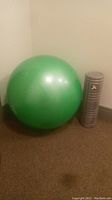 Green inflated yoga exercise ball next to grey foam roller standing upright against wall on carpet