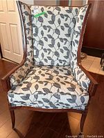 Front view showing wing back design, leaf patterned upholstery, wood trim details, and tufted seat cushion.