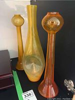 Three glass art vases in orange, yellow, and amber colors, showing height and shape variety