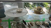 Two white ceramic cake stands displayed on a surface with a variety of silverware in front, Royal Doulton Bunnykins 4 piece set placed on one cake stand, small Bavaria trinket dish on the other stand.