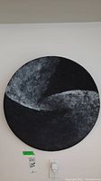 Full view of the round black and gray abstract wall art plate hanging on a white wall with an electrical outlet below it.