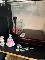Shelf display of items including coalport figurine, ceramic shoes, wooden tea box, and ceramic spoons