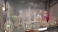 Shelved group of six crystal decanters and one pink-tinted glass vase, showing variety of shapes and sizes