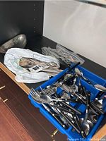 Overview of assortment of cutlery in blue tray and a metal serving bowl partially visible to the side.