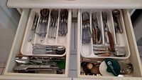 View of two drawers showing clear handled cutlery including forks, spoons, knives, and metal tongs and kitchen scissors with wooden handles