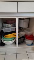 Full view of cabinet interior showing stacked food storage containers, enamel stock pots, cake pans, and other kitchen utensils.