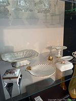 Overview of the fine bone china set including trays, trinket boxes, cup and saucer, dinner bell, and stone covered box on a shelf
