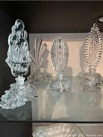 Four ornate clear glass perfume bottles with decorative cut glass stoppers and bases, arranged side by side on a shelf.