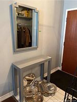 Grey laminate Parsons hall table with clean rectangular silhouette and matching grey laminate wall mirror with stepped corner detail, both near an entry door.