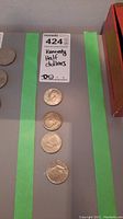 Four Kennedy half dollars arranged vertically on a grey surface with a lot label beside them.