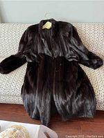 Black full length mink fur coat spread out on a couch showing the front side with collar and sleeves.