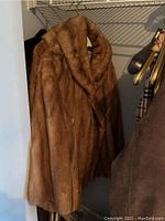 Brown mink fur coat hanging in closet showing full front and sides.