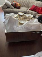 Overall view showing coffee table in living room setting with draped cloth and stacked china dishes.