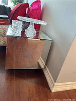 Square mirrored side table placed against a wall with some decorative items on top. Shows overall design and condition.